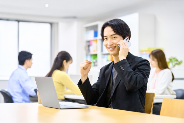 電話をしながらガッツポーズをする若い男性